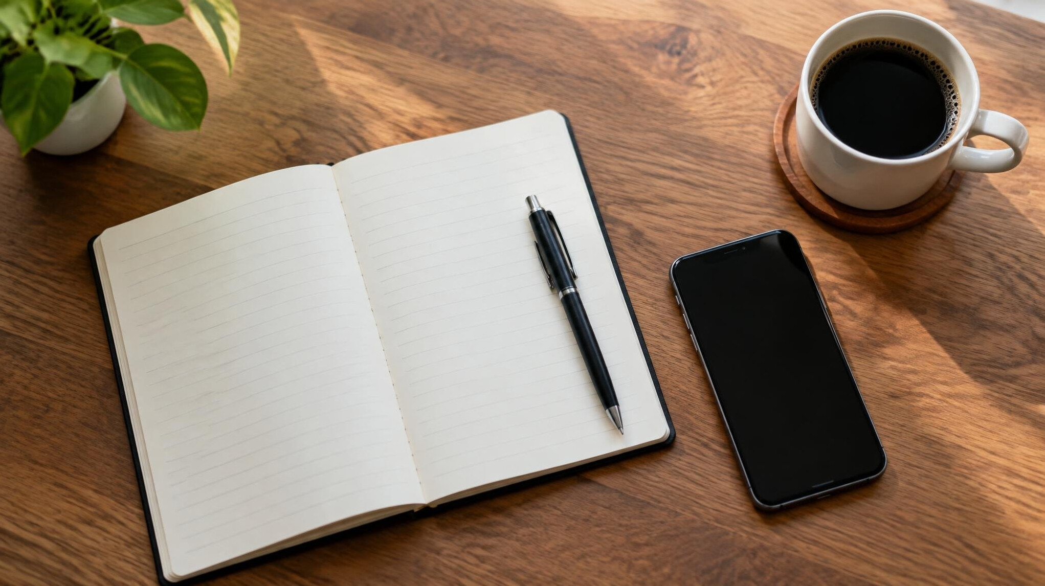 Open notebook with a pen next to a smartphone and cup of coffee